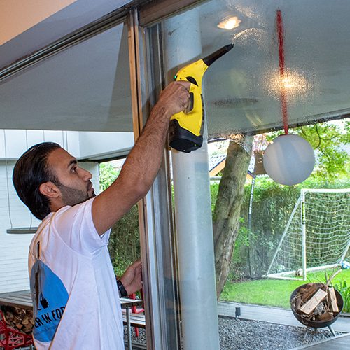 grund_Fensterreinigung-sauber_in_form Ein Mitarbeiter von Sauber In Form reinigt die Fensterscheiben eines Gebäudes mit einem Dampfreiniger.