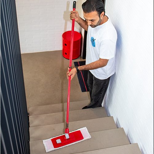treppenhausreinigung-sauber_in_form-01 Ein Mitarbeiter von Sauber In Form reinigt sorgfältig die Treppen mit einem roten Wischmopp.